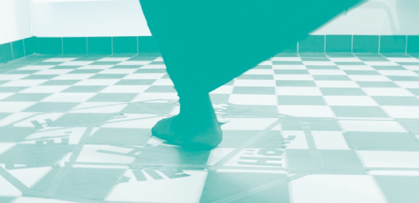 Grün gefärbtes Bild. Ein Fuß in flachem Tanzschuh auf einem Boden im Schachbrettmuster.